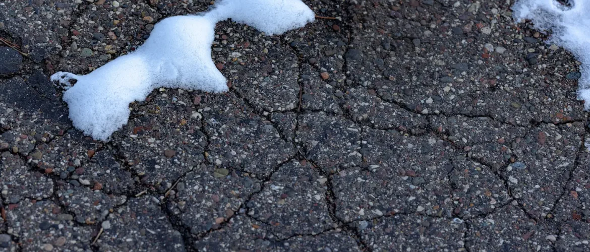 Closeup of cracked and crumbling asphalt with snow